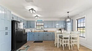 Una cucina moderna con mobili azzurri, un frigorifero nero e un'area pranzo con sedie bianche.