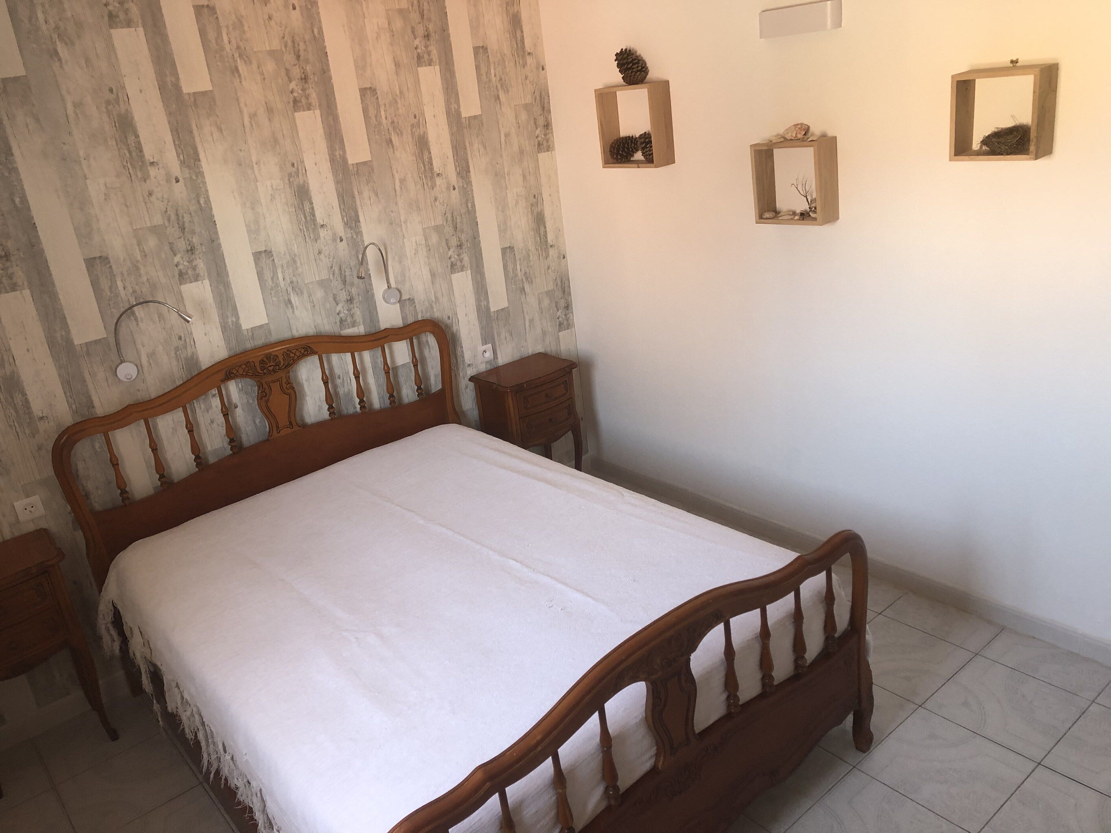A bedroom with a wooden bed, a nightstand, and a wall-mounted shelf with decorative items.