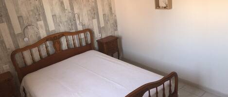 A bedroom with a wooden bed, a nightstand, and a wall-mounted shelf with decorative items.