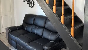 Een zwarte leren bank, een houten trap en een klok aan de muur.