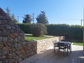 Un patio con muro de piedra, terraza de madera y una mesa con sillas.