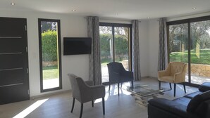 Un soggiorno spazioso con una grande TV, due poltrone, un divano e un tavolino in vetro.