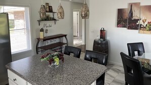 A modern kitchen with granite countertops, hanging pendant lights, and a dining area with a bench and chairs.