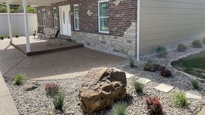 A residential house with a covered patio, a brick exterior, and a landscaped garden with rocks and small plants.