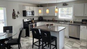 A modern kitchen with white cabinets, a granite countertop, a central island with chairs, a microwave, a stove, and pendant lights.
