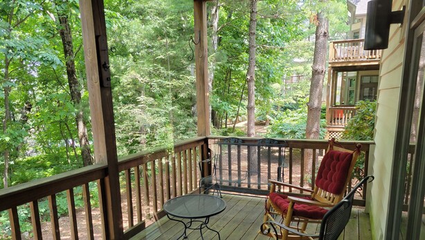 A wooden deck with a table and two chairs, surrounded by trees.