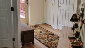 A hallway with wooden flooring, a patterned rug, a wicker bench, and a door with a 'SKI' sign.