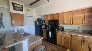 A kitchen with wooden cabinets, granite countertops, a refrigerator, a microwave, and a stove.