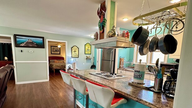 A kitchen with a bar area, wooden flooring, and a refrigerator. - Book Fast! Top-Rated 5★ Cottage Near Carolina Beach—Private, Peaceful, Perfect (Wilmington)