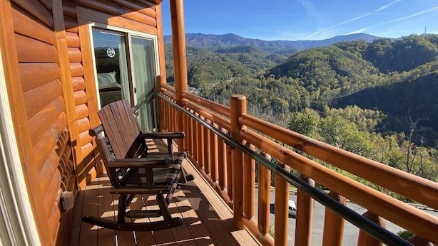 A wooden deck with a rocking chair and a table, overlooking a mountainous landscape.