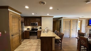 A modern kitchen with wooden cabinets, a central island, and a dining area with chairs.