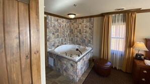 A bathroom with a stone wall, a bathtub, a wooden door, and a small round stool.