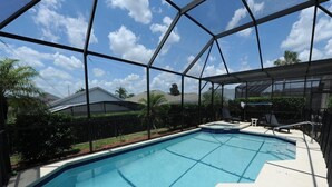 A swimming pool with a clear blue water, surrounded by a glass enclosure, and a small hot tub. - Windsor Palms 48 (Kissimmee)