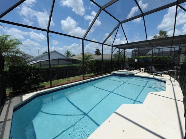 A swimming pool with a clear blue water, surrounded by a glass enclosure, and a small hot tub. - Windsor Palms 48 (Kissimmee)