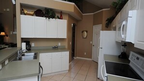 A kitchen with white cabinets, a sink, a stove, and a microwave. - Windsor Palms 48 (Kissimmee)