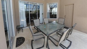 A glass-top dining table with six chairs, a ceiling fan, and a sliding glass door leading to an outdoor area. - Windsor Palms 48 (Kissimmee)