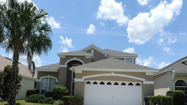 A two-story house with a single garage, surrounded by well-maintained lawns and palm trees. - Windsor Palms 48 (Kissimmee)