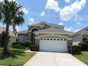 A two-story house with a single garage, surrounded by well-maintained lawns and palm trees. - Windsor Palms 48 (Kissimmee)