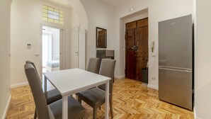 Un coin repas avec une table et des chaises blanches, un plancher en bois, un réfrigérateur et une porte dotée d’un miroir.