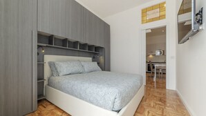 Une chambre comprenant un lit, des étagères intégrées, un bureau et un coin cuisine.