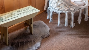 A cozy room with a wooden floor, a bench, a macramé hanging chair, and a window with curtains. - PRIME Location~Walk to Ski Shuttle ~ Fully Fenced ~ EV Charger ~ Mini Sled Hill (Big Bear Lake)