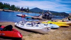 A row of kayaks and a red jet ski on a sandy beach with a body of water and a dock in the background. - PRIME Location~Walk to Ski Shuttle ~ Fully Fenced ~ EV Charger ~ Mini Sled Hill (Big Bear Lake)