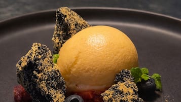 Un postre con una bola de helado, frutos rojos y un plato oscuro.