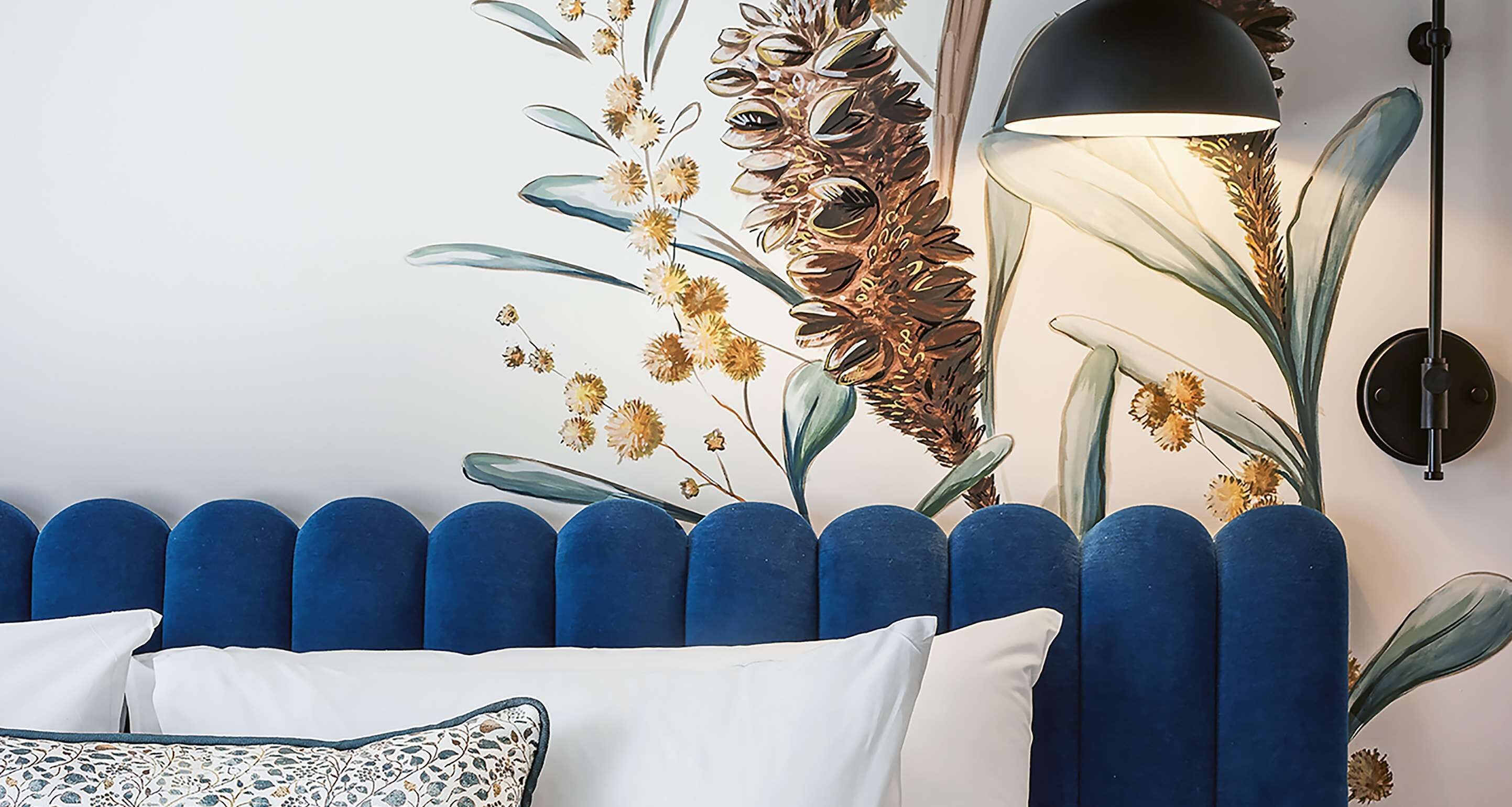 Ein Zimmer mit einem blau gepolsterten Kopfteil, einem weißen Kissen und einer Wandlampe.
