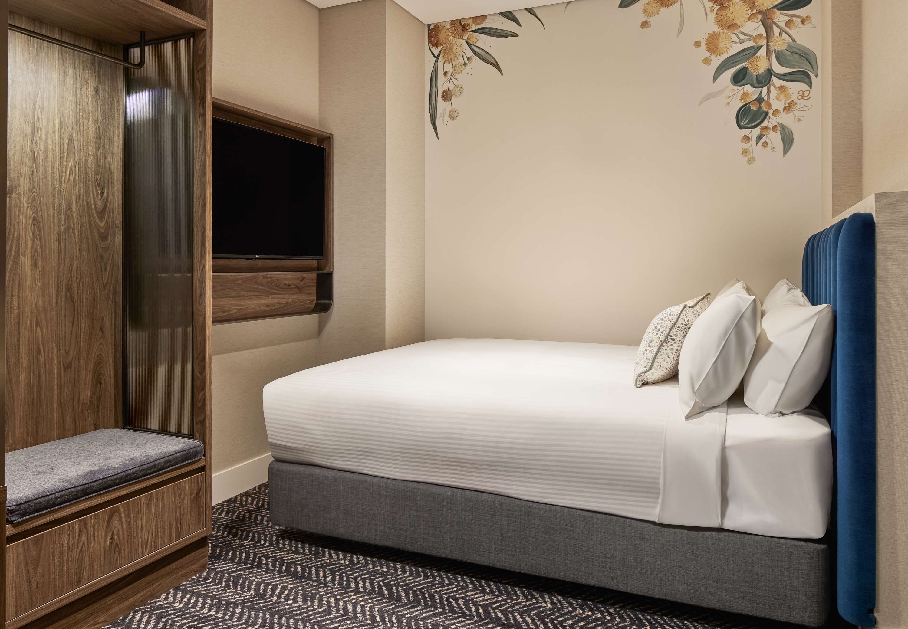 A bedroom with a bed, a TV, a wardrobe, and a patterned rug.