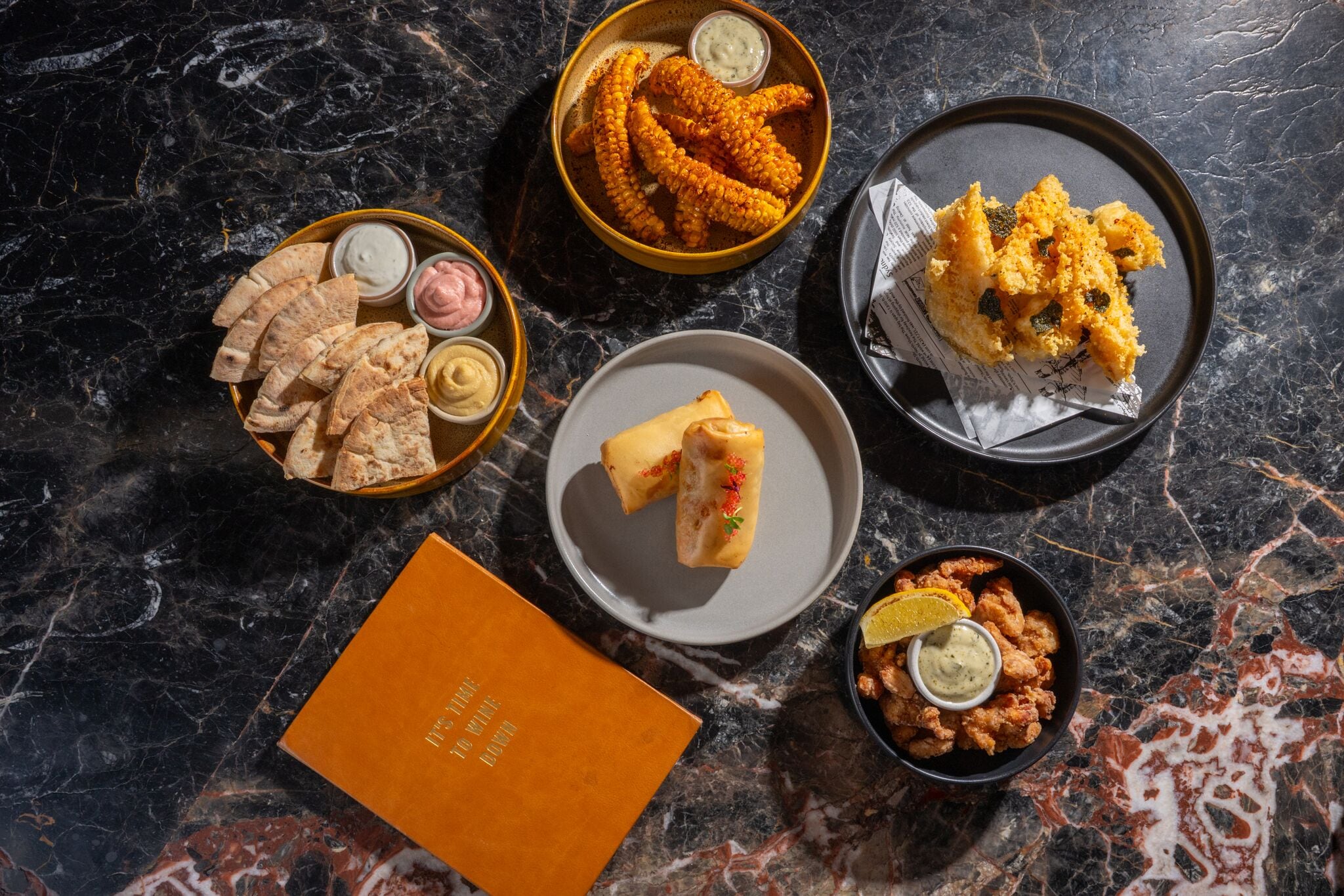 A variety of food items on a marble surface, including fried items and bread.