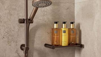 A shower with a handheld showerhead and a wall-mounted shelf holding three bottles of hair care products.