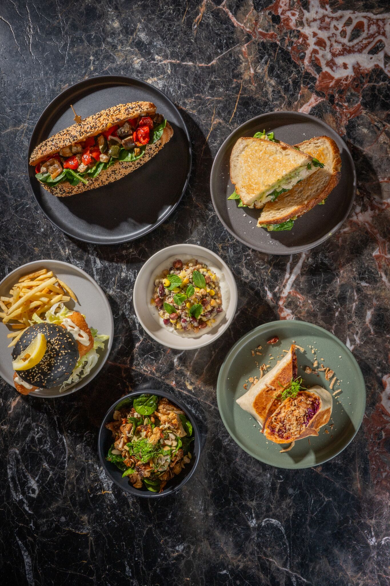 Variedad de platillos en los platos, incluyendo un sándwich, papas fritas y una ensalada.