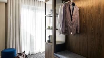 Habitación de hotel con armario de madera, un banco, un otoman azul y perchero.