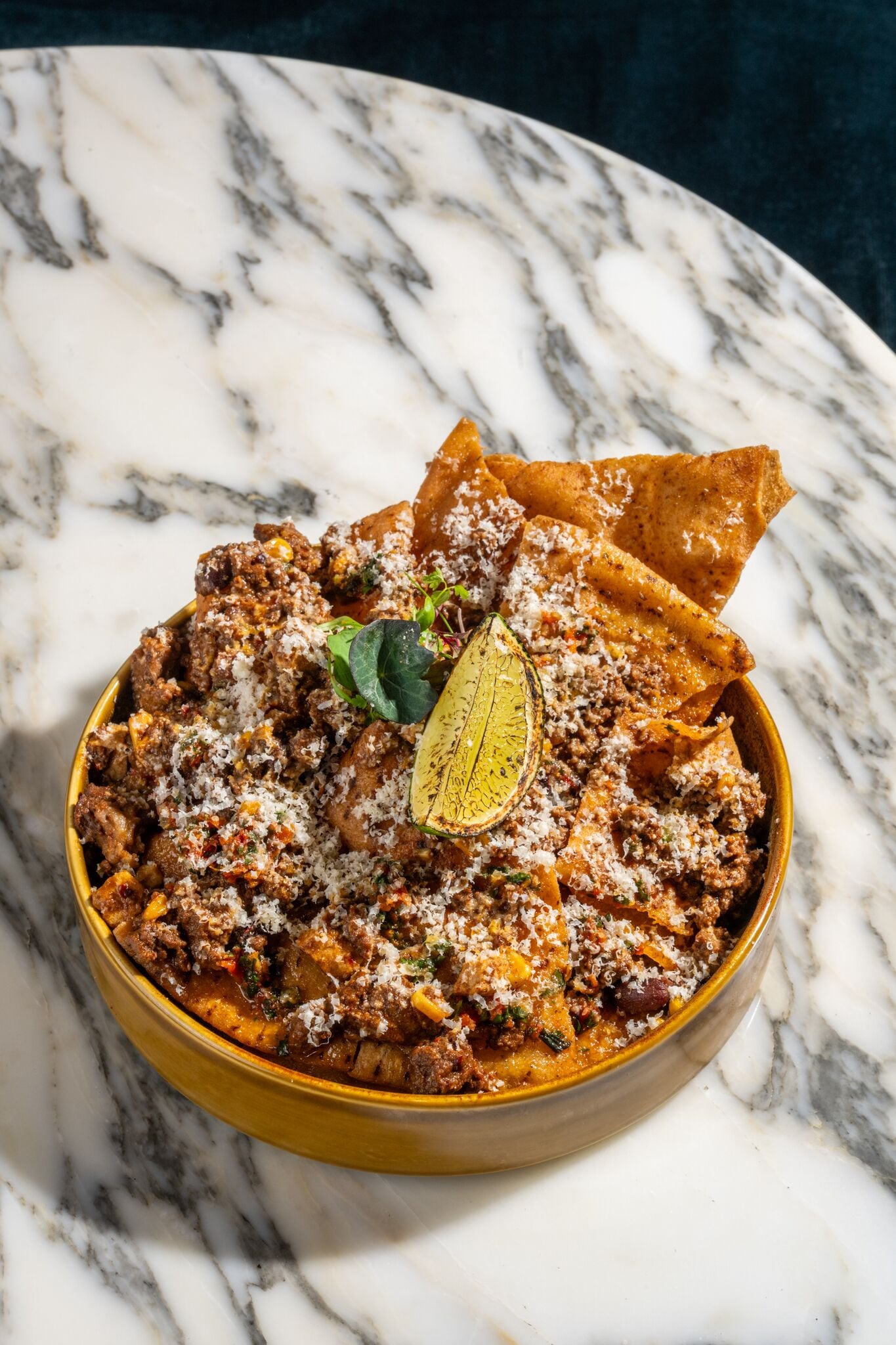 Eine Schüssel Chili mit Tortilla-Chips und einer Limettenspalte auf einer Marmorplatte.