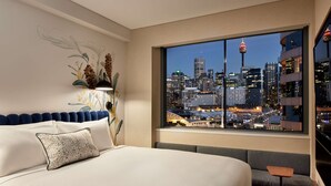 Ein Hotelzimmer mit einem großen Bett, Blick auf eine Stadtlandschaft und einem durch das Fenster sichtbaren Stadtpark.