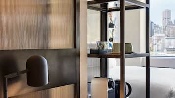 Ein modernes Hotelzimmer mit Schreibtisch aus Holz, einem Laptop, einer Kaffeemaschine und einem Bücherregal.