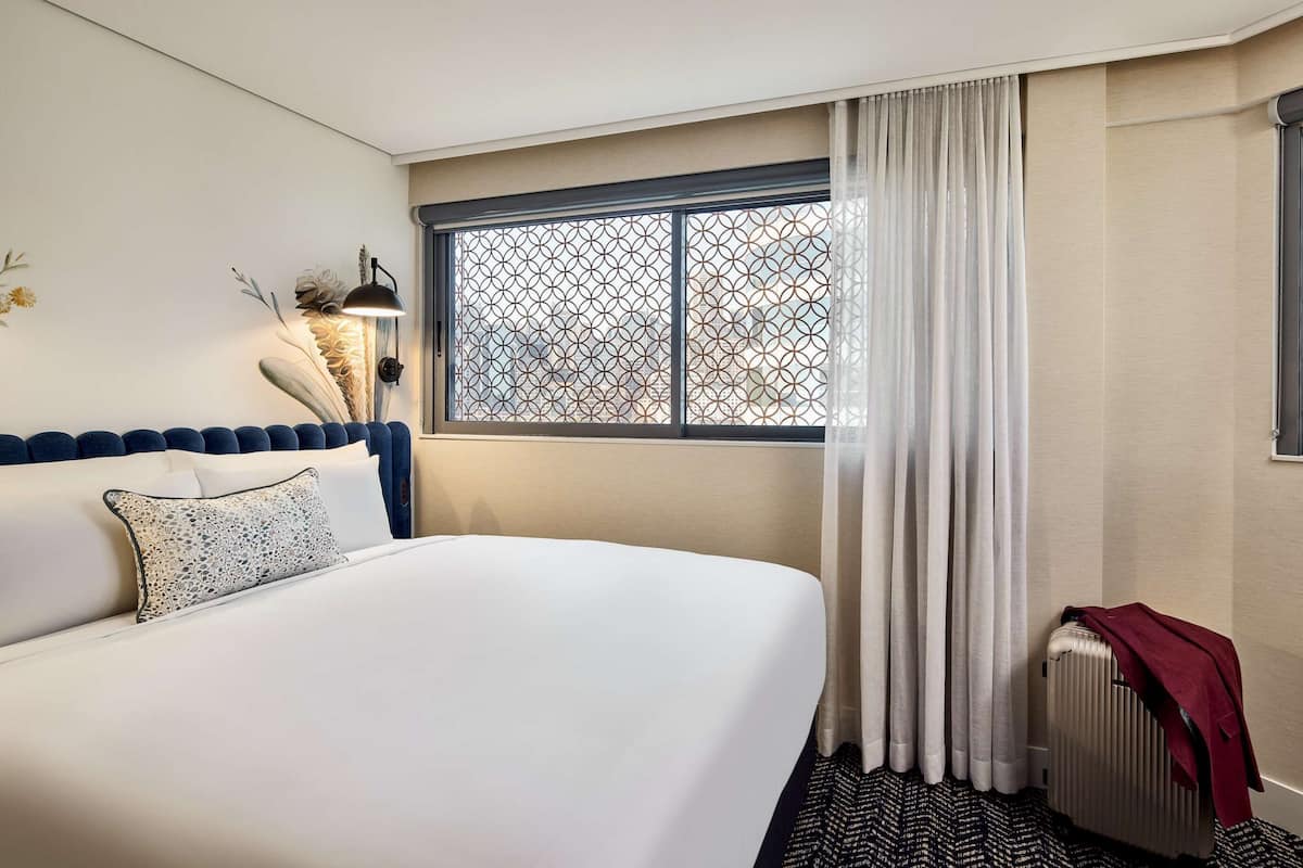 A hotel room with a large bed, a radiator, and a window with a geometric pattern.