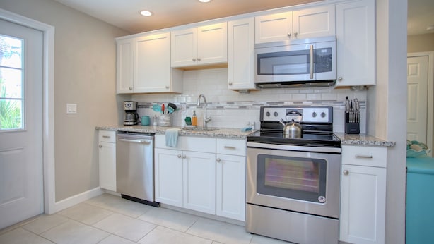 A modern kitchen with white cabinets, stainless steel appliances, and a tiled backsplash. - Casa de playa walk to the beach (Ormond Beach)