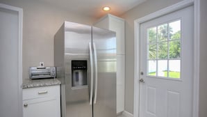 A kitchen with a stainless steel refrigerator, a built-in toaster oven, and a window with a view of greenery. - Casa de playa walk to the beach (Ormond Beach)