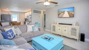 A living room with a ceiling fan, a television, a sofa with decorative pillows, and a cabinet with decorative items. - Casa de playa walk to the beach (Ormond Beach)