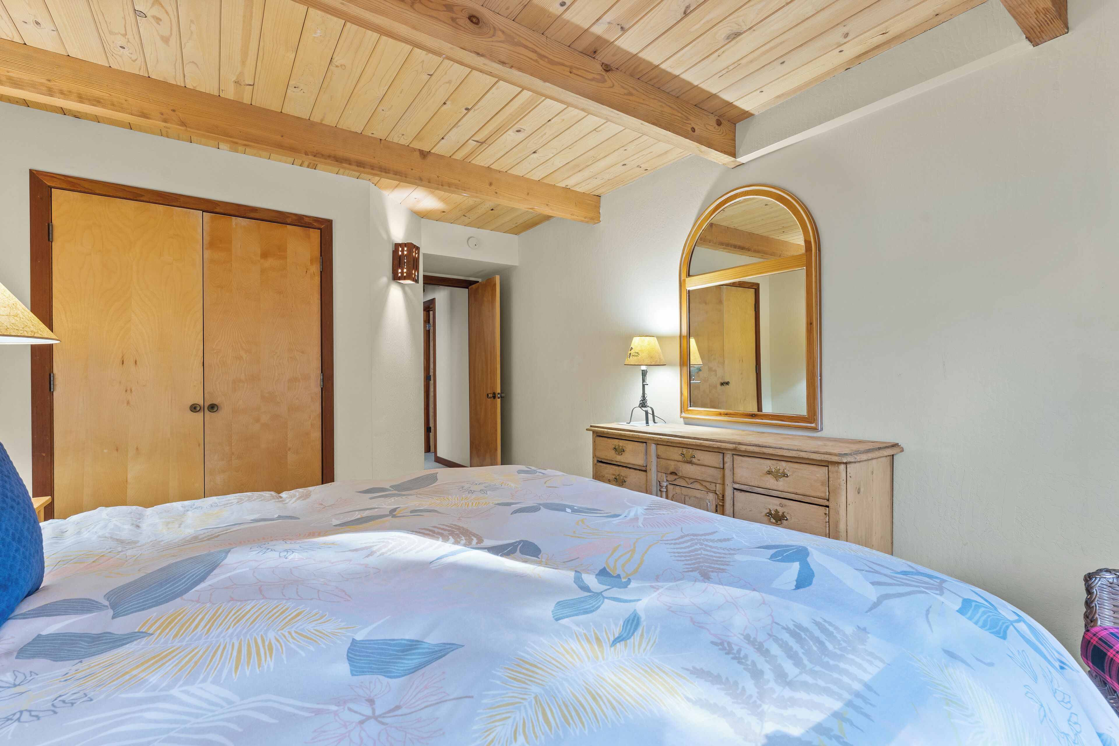 Un dormitorio con cama, armario de madera, cómoda y espejo.