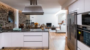 A modern kitchen with a large island, stone wall, and a built-in oven. - Casa Quinta Do Rio (Braga)