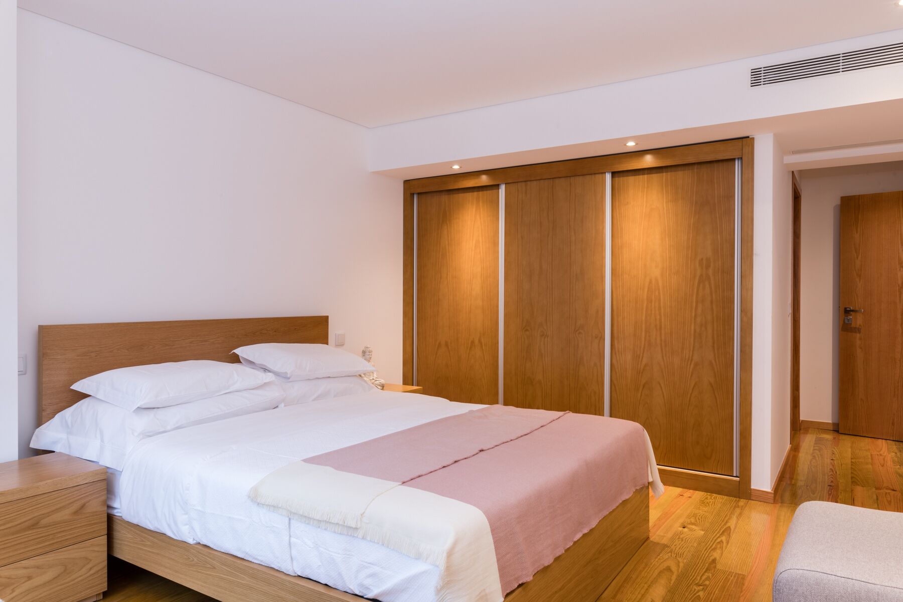 Une chambre à coucher avec un lit en bois, une table de chevet, une armoire et une porte donnant sur une autre pièce.