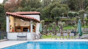 A poolside area with a small building, outdoor seating, and a view of trees and hills. - Casa Quinta Do Rio (Braga)