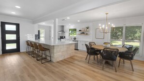 Una cucina moderna con isola centrale, sgabelli da bar, un tavolo da pranzo con sedie e un lampadario.