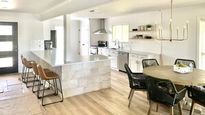 Una cucina moderna con isola centrale, sgabelli da bar, un tavolo da pranzo con sedie e un lampadario.