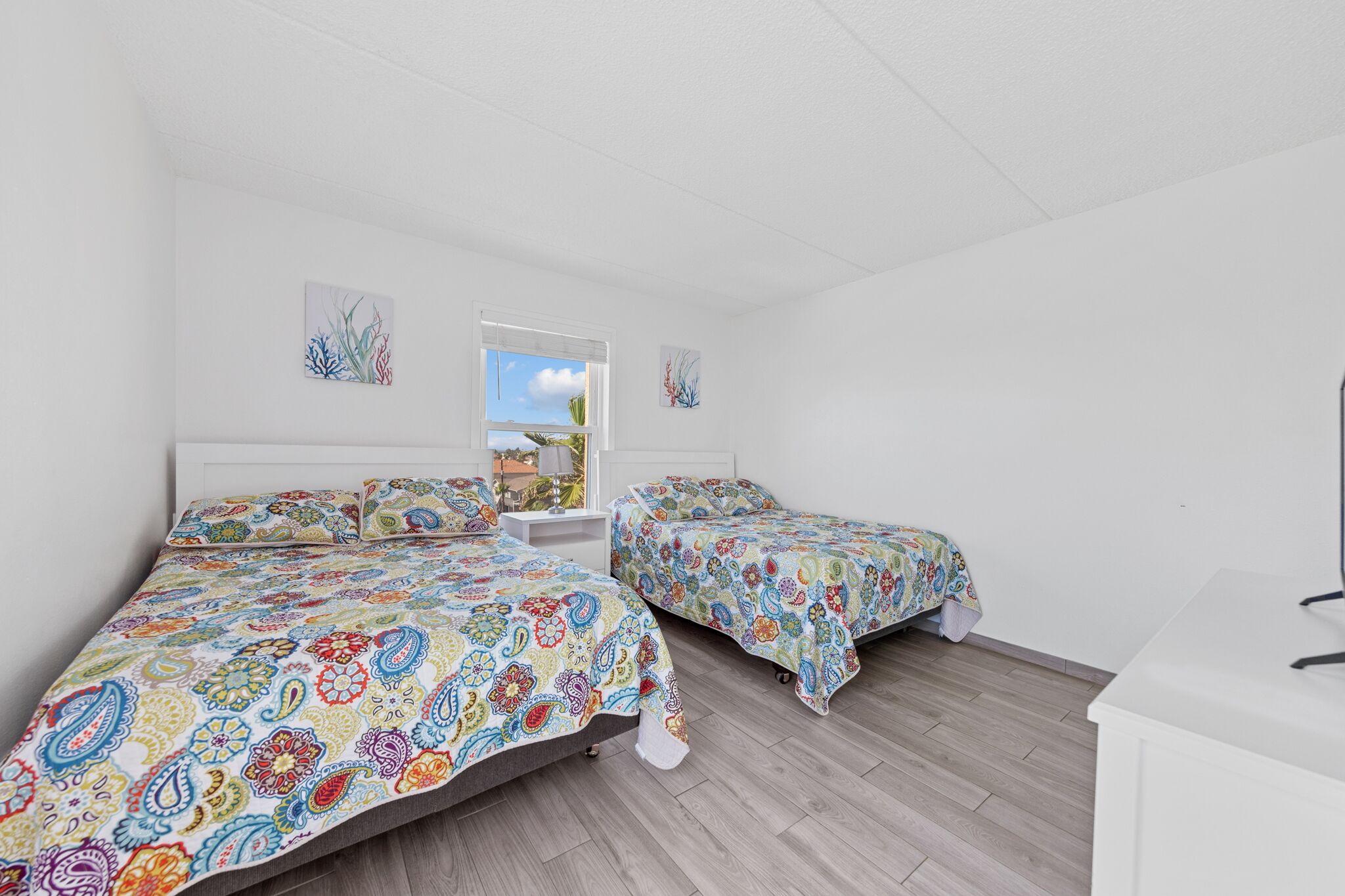 A bedroom with two beds, a window, and artwork on the walls.