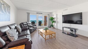 Un soggiorno moderno con un divano in pelle, un tavolino in legno, una televisione a schermo piatto e un balcone con vista sul mare.