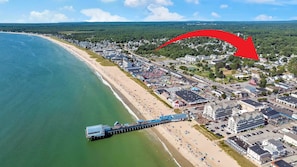 An aerial view of a coastal town with a pier extending into the water, surrounded by buildings and a beach.