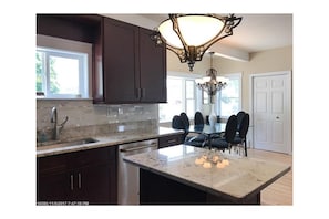 A kitchen with dark wooden cabinets, a granite countertop, a dining table with chairs, and a chandelier.